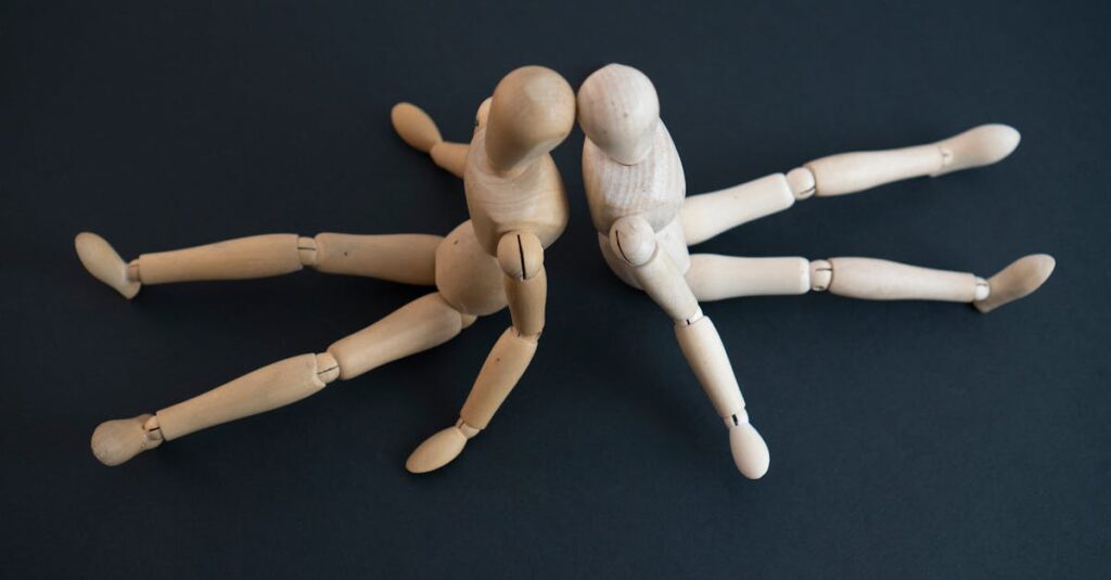 Close-up of wooden artist mannequins sitting on a dark surface, posing together.