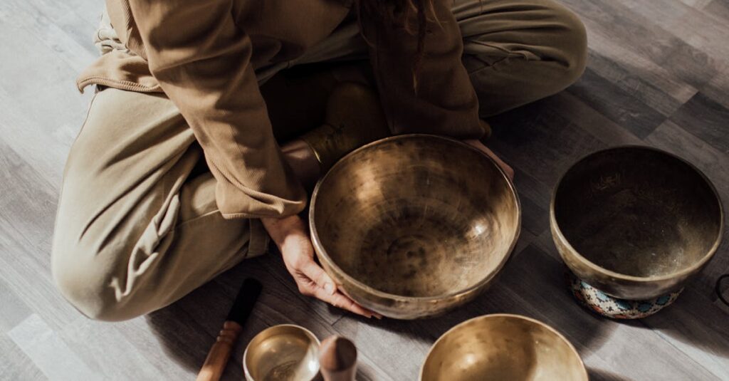 A person meditates with Tibetan singing bowls on a wooden floor, creating a serene atmosphere.